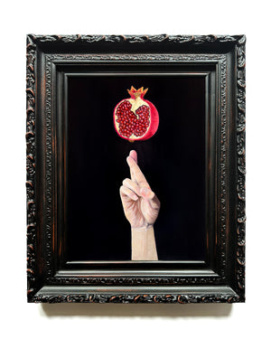 Framed hand with a cracked pomegranate against a black background