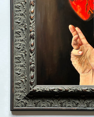 Close up artistic depiction of a hand holding a glowing red heart against a dark background, framed in ornate black wood.