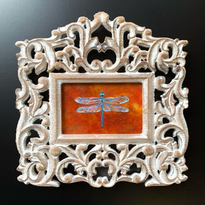blue and orange dragonfly painting in ornate white wood frame