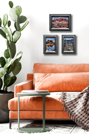 3 small desert landscape paintings in silver frames hanging on wall next to cactus