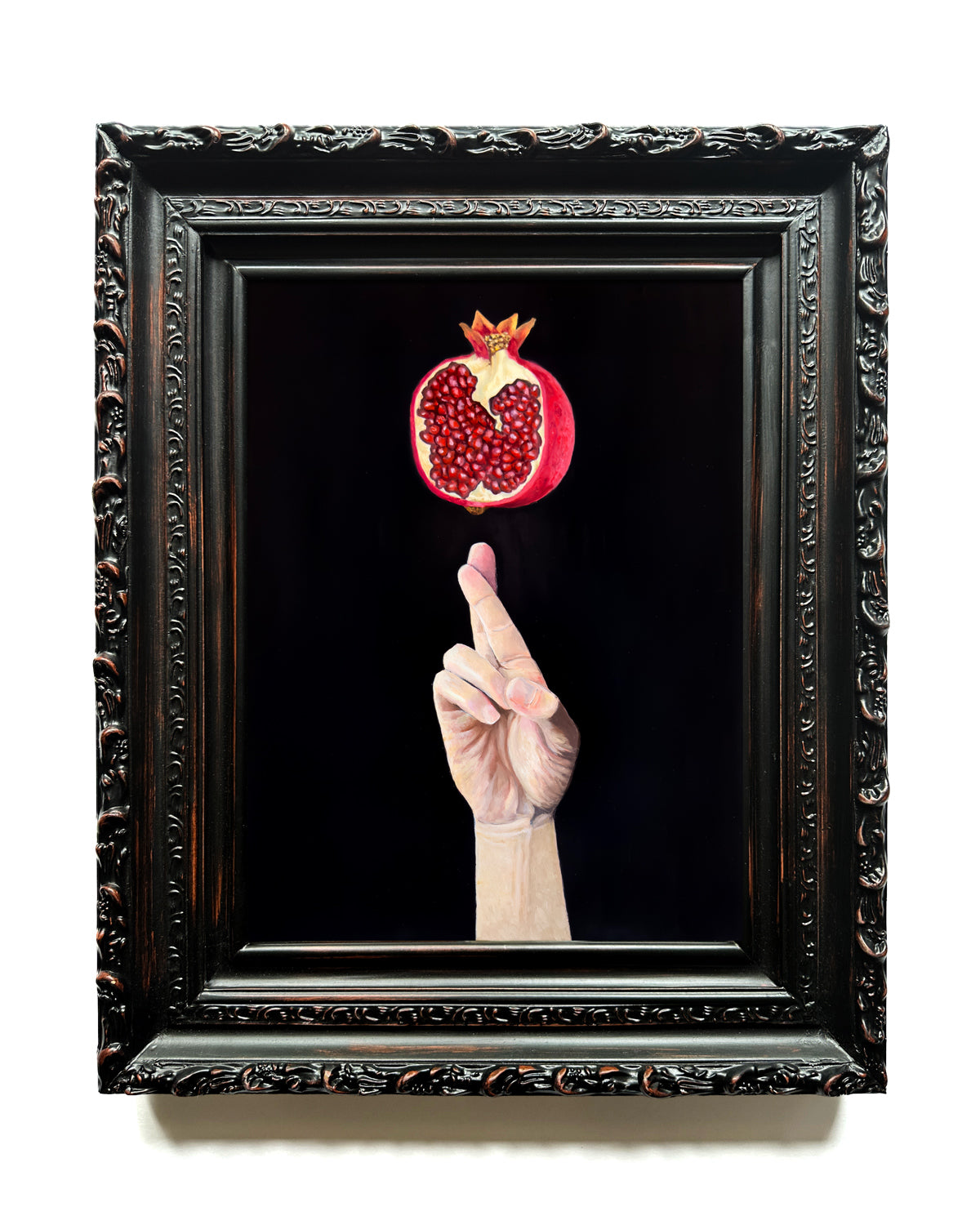 Framed hand with a cracked pomegranate against a black background