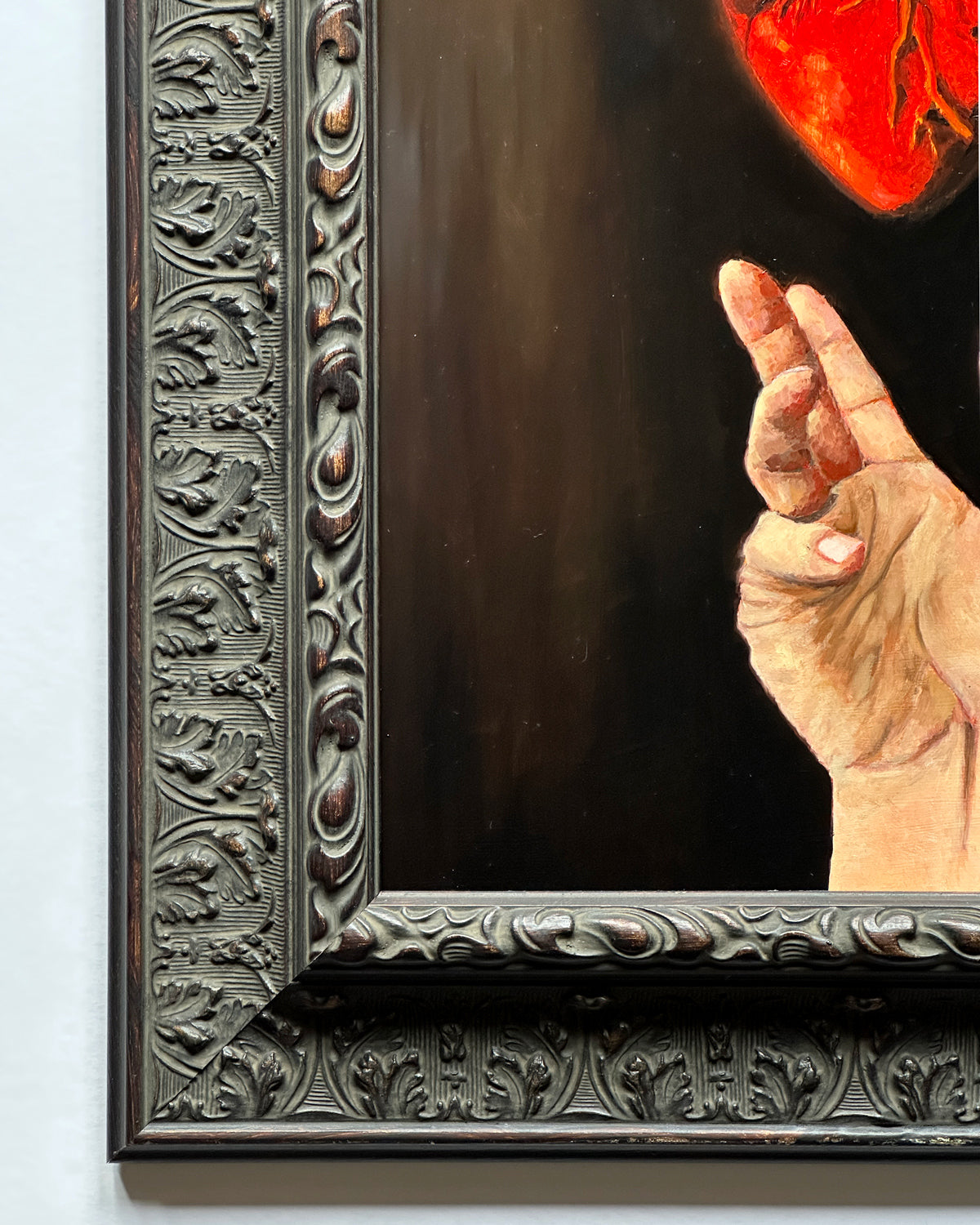 Close up artistic depiction of a hand holding a glowing red heart against a dark background, framed in ornate black wood.