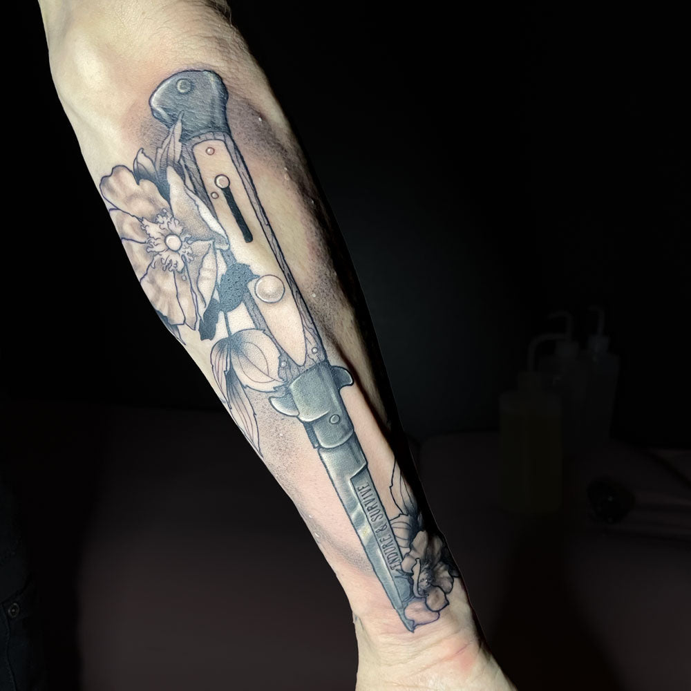 knife and floral tattoo on forearm by Cass Brown